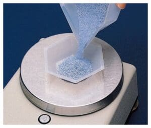 Pouring granular material onto a hexagonal mold on a metallic base.